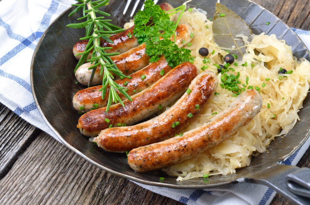 Bratwürste auf Sauerkraut in einer Pfanne, garniert mit Kräutern.