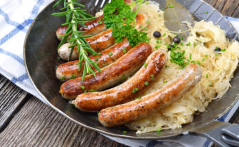 Bratwürste auf Sauerkraut in einer Pfanne, garniert mit Kräutern.