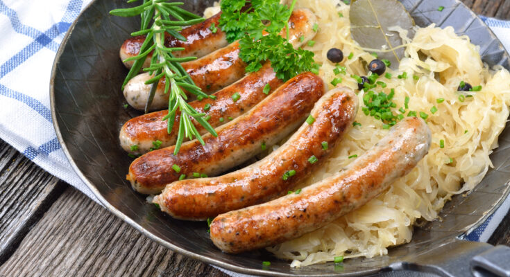 Bratwürste auf Sauerkraut in einer Pfanne, garniert mit Kräutern.