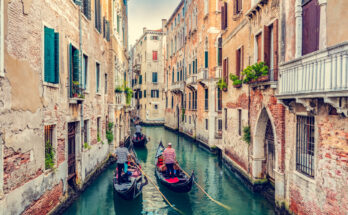 Gondolieri steuern drei Gondeln durch einen schmalen Kanal in Venedig, flankiert von verwitterten Backsteinfassaden mit Balkonen und Fensterläden.