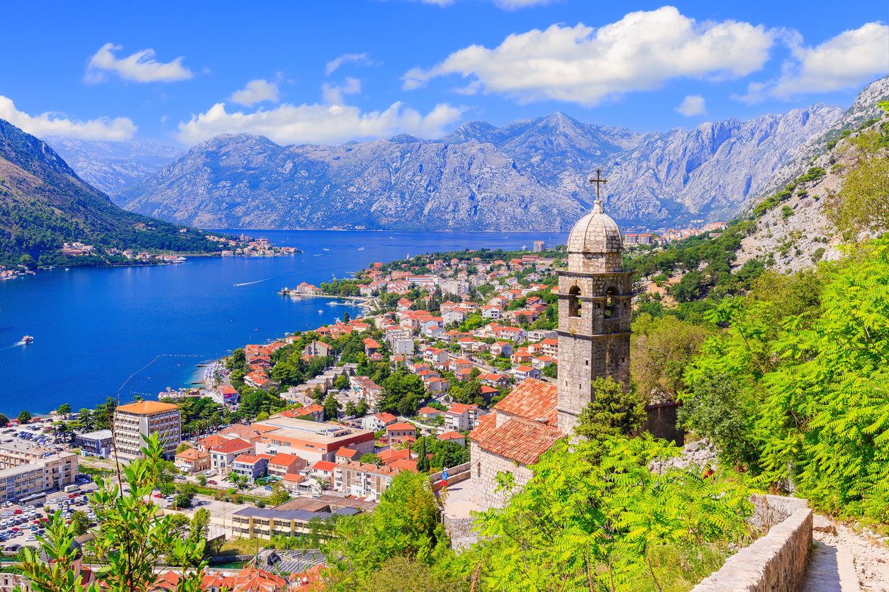 Panorama von Kotor in Montenegro mit Kirchturm über roten Ziegeldächern und der Bucht von Kotor vor steilen Bergen.