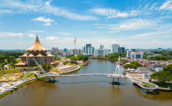 Luftaufnahme der geschwungenen Darul-Hana-Brücke vor dem goldenen Parlamentsgebäude in Kuching.
