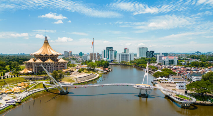 Luftaufnahme der geschwungenen Darul-Hana-Brücke vor dem goldenen Parlamentsgebäude in Kuching.