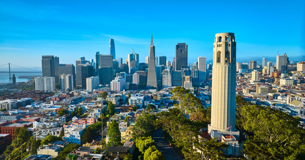 Der Coit Tower steht auf Telegraph Hill vor der Skyline von San Francisco mit Transamerica Pyramid, Salesforce Tower und Bay Bridge.