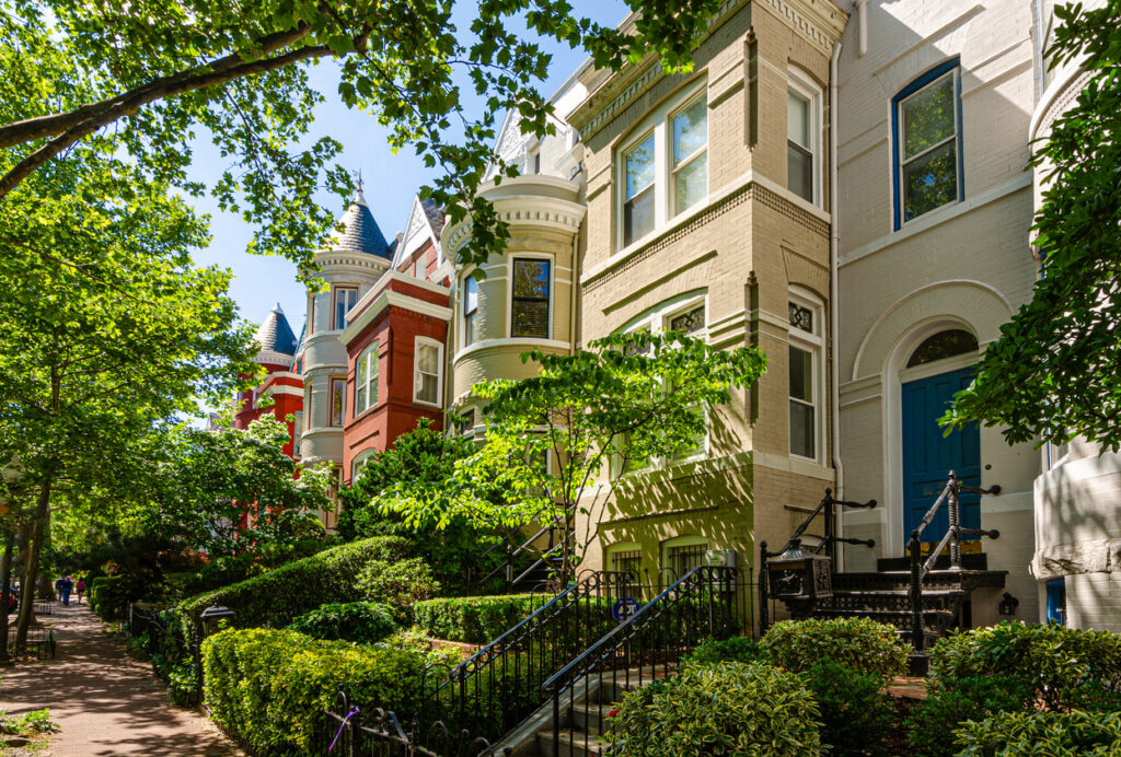 Bunte viktorianische Rowhouses mit Erkern und Türmchen in Georgetown, Washington, D.C., entlang eines schattigen Gehwegs mit üppigen Vorgärten.