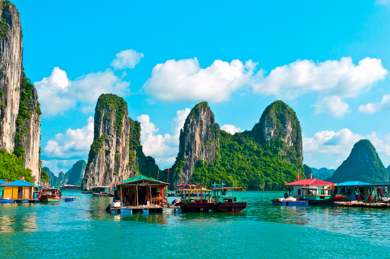 Bunte Boote und schwimmende Häuser vor grünen Karstfelsen in der Halong-Bucht, Vietnam.