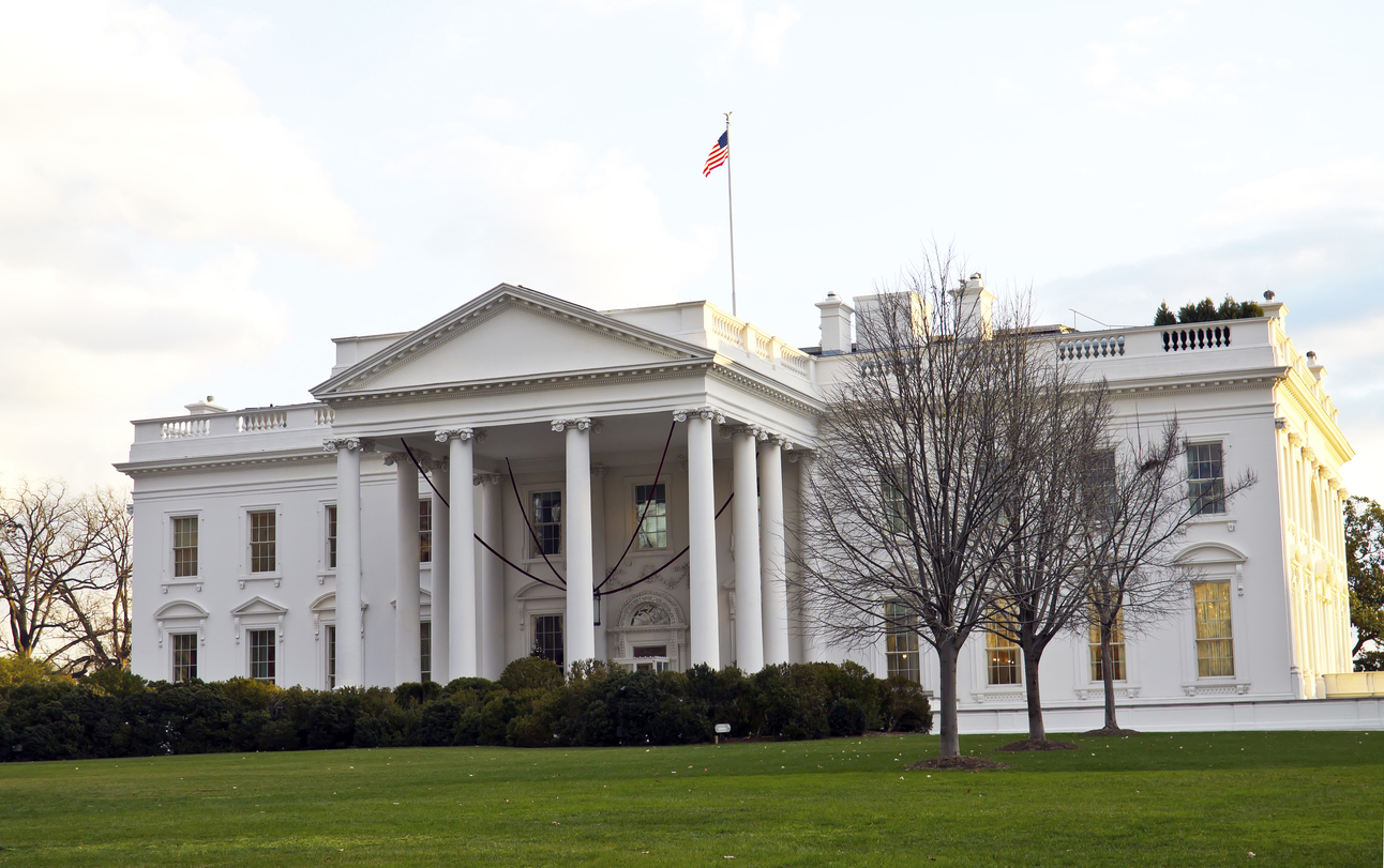 Frontansicht des Weißen Hauses (Nordseite) mit Säulen, US-Flagge und kahlen Bäumen auf dem Rasen in Washington, D.C.