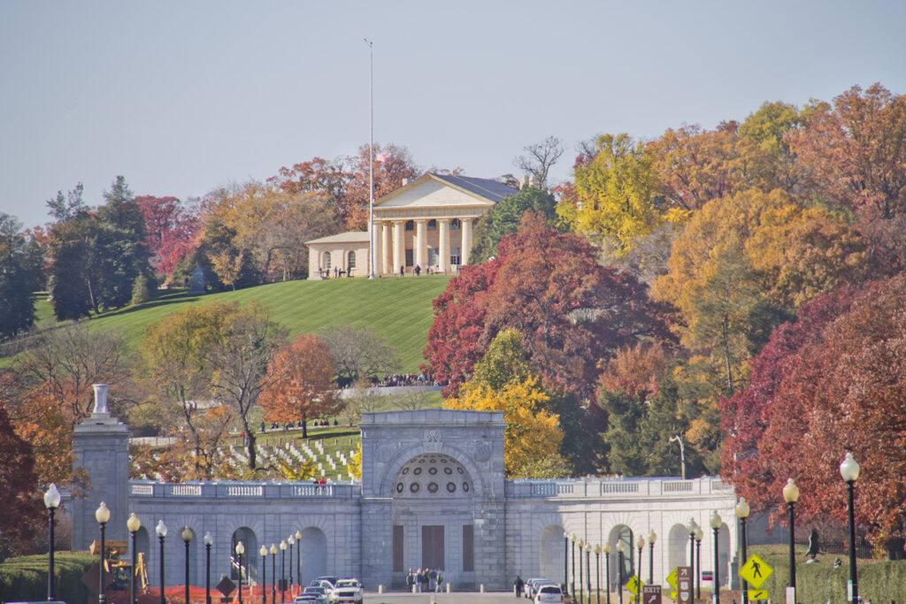 Eingangstor und Grabfelder des Arlington National Cemetery mit Arlington House auf dem Hügel, umgeben von buntem Herbstlaub nahe Washington, D.C.