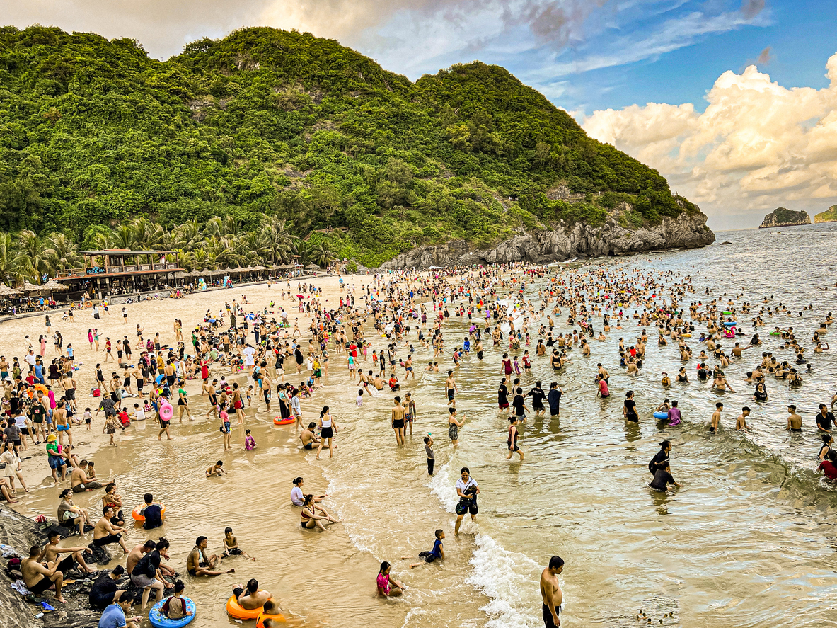 Zahlreiche Menschen baden und entspannen an einem belebten Strand auf Cat Ba Island.