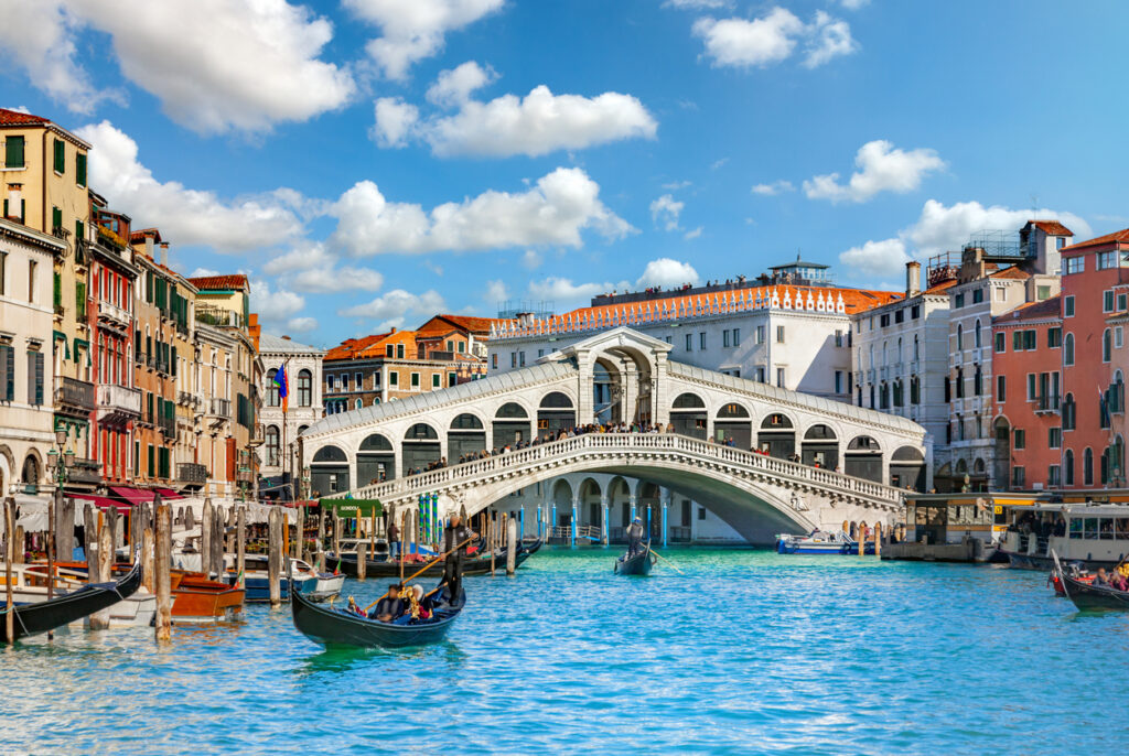 Die Rialtobrücke in Venedig spannt sich über den Canal Grande, umgeben von historischen Palazzi und Gondeln auf türkisblauem Wasser.