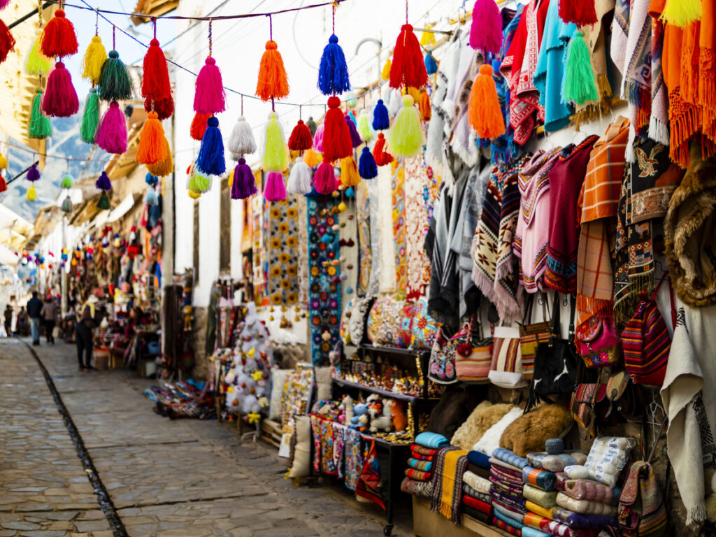Eine schmale Gasse in Cusco zeigt farbige Quasten und Stände voller Ponchos, Taschen und Decken.