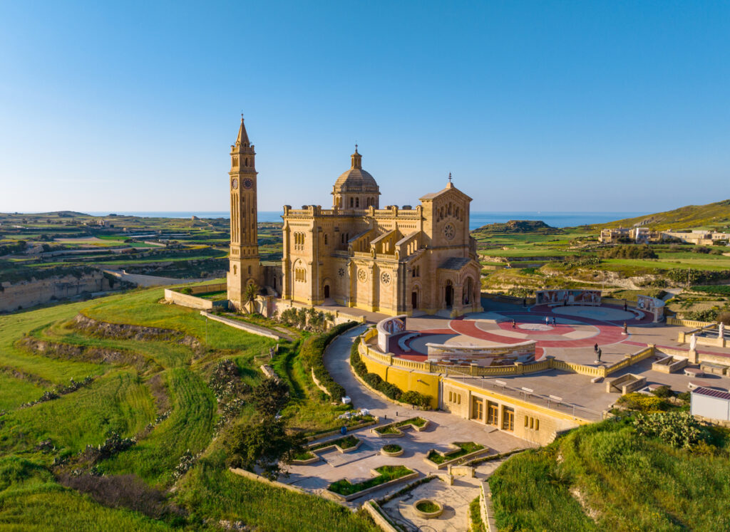 Luftaufnahme der Basilika Ta’ Pinu bei Għarb auf Gozo mit Vorplatz, Gärten und Meer im Hintergrund.