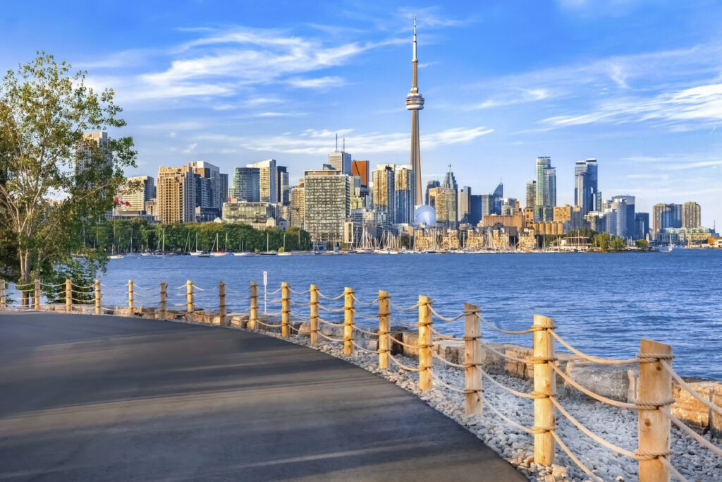 Von einer Uferpromenade aus sieht man Torontos Skyline mit dem CN Tower über dem Hafen.