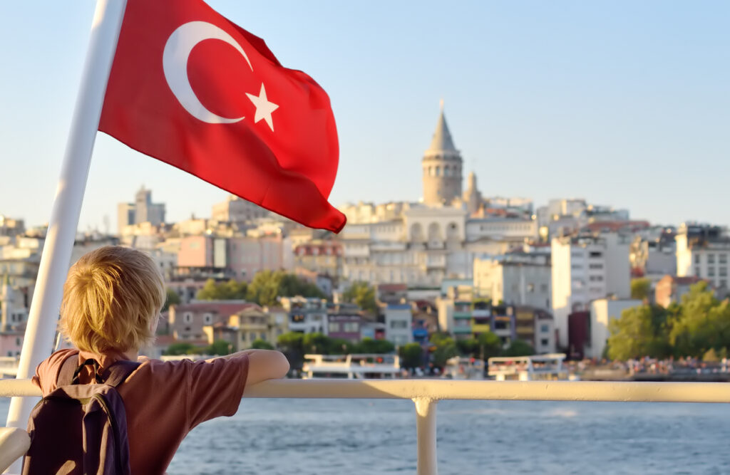 Junge schaut von der Fähre auf Istanbul, die Türkei-Flagge weht.