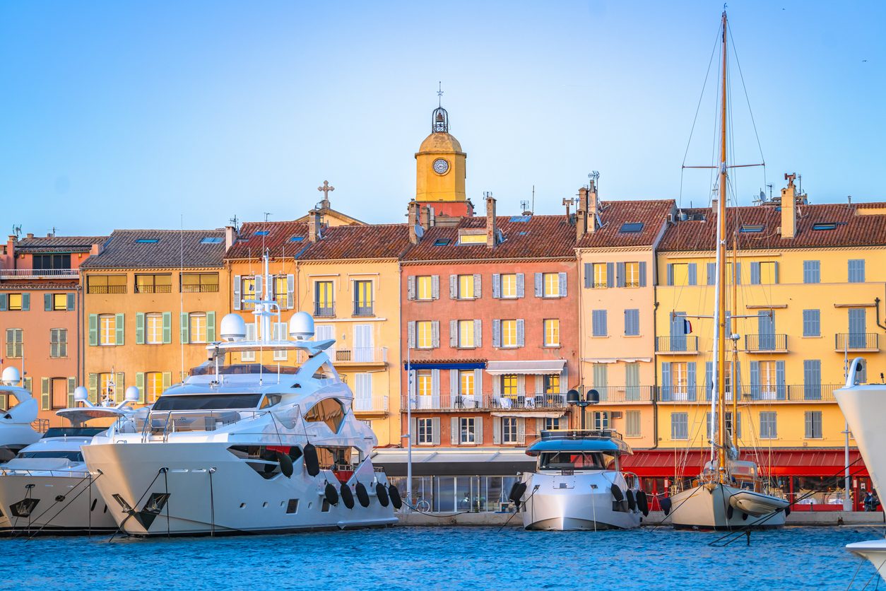 Luxusyachten im Hafen von Saint-Tropez vor bunten Altstadthäusern und markantem Uhrturm im warmen Abendlicht.
