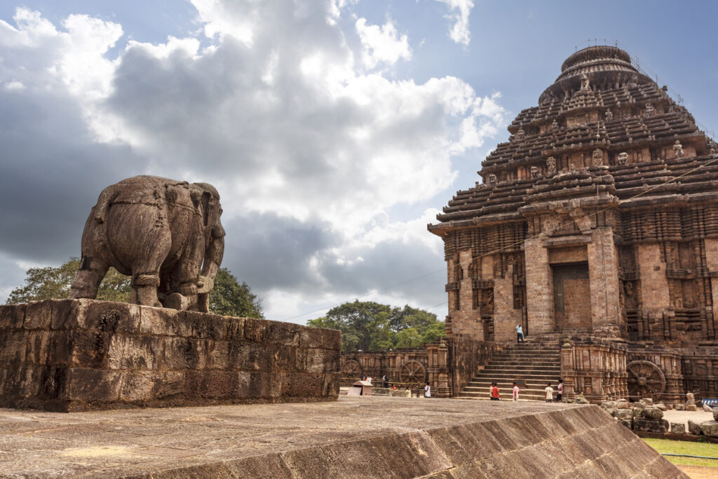 Der Sun Temple von Konark in Odisha zeigt reich verzierte Sandsteinfassaden mit Wagenrädern, Treppe und monumentaler Elefantenstatue unter dramatischem Himmel.