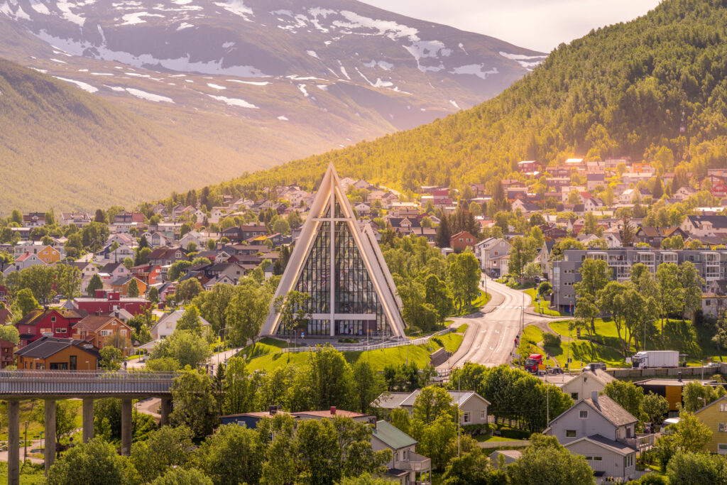 Panorama von Tromsø mit der markanten Eismeerkathedrale (Ishavskatedralen) in Tromsdalen, umgeben von bunten Häusern und Bergkulisse.
