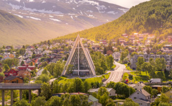Panorama von Tromsø mit der markanten Eismeerkathedrale (Ishavskatedralen) in Tromsdalen, umgeben von bunten Häusern und Bergkulisse.