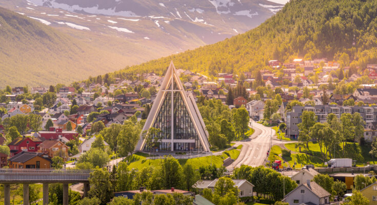 Panorama von Tromsø mit der markanten Eismeerkathedrale (Ishavskatedralen) in Tromsdalen, umgeben von bunten Häusern und Bergkulisse.