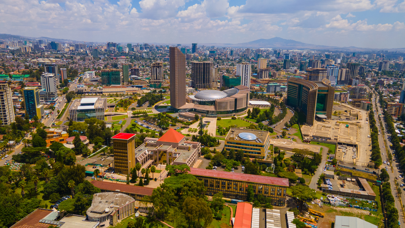 Luftaufnahme von Addis Abeba, Äthiopien: zentral der Hauptsitz der Afrikanischen Union mit rundem Plenarbau und hohem Turm, umgeben von modernen Hochhäusern, Straßen und Grünflächen; im Hintergrund breitet sich die Stadt bis zu den Entoto-Bergen aus.