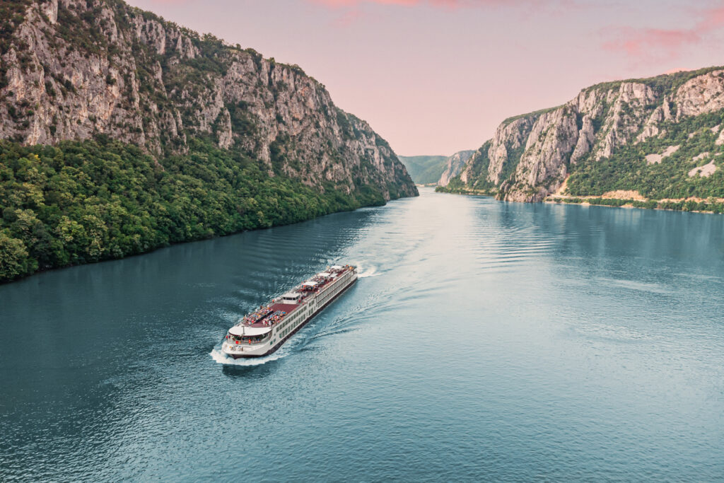 Ein Flusskreuzfahrtschiff fährt durch eine enge Donauschlucht mit bewaldeten Felswänden.