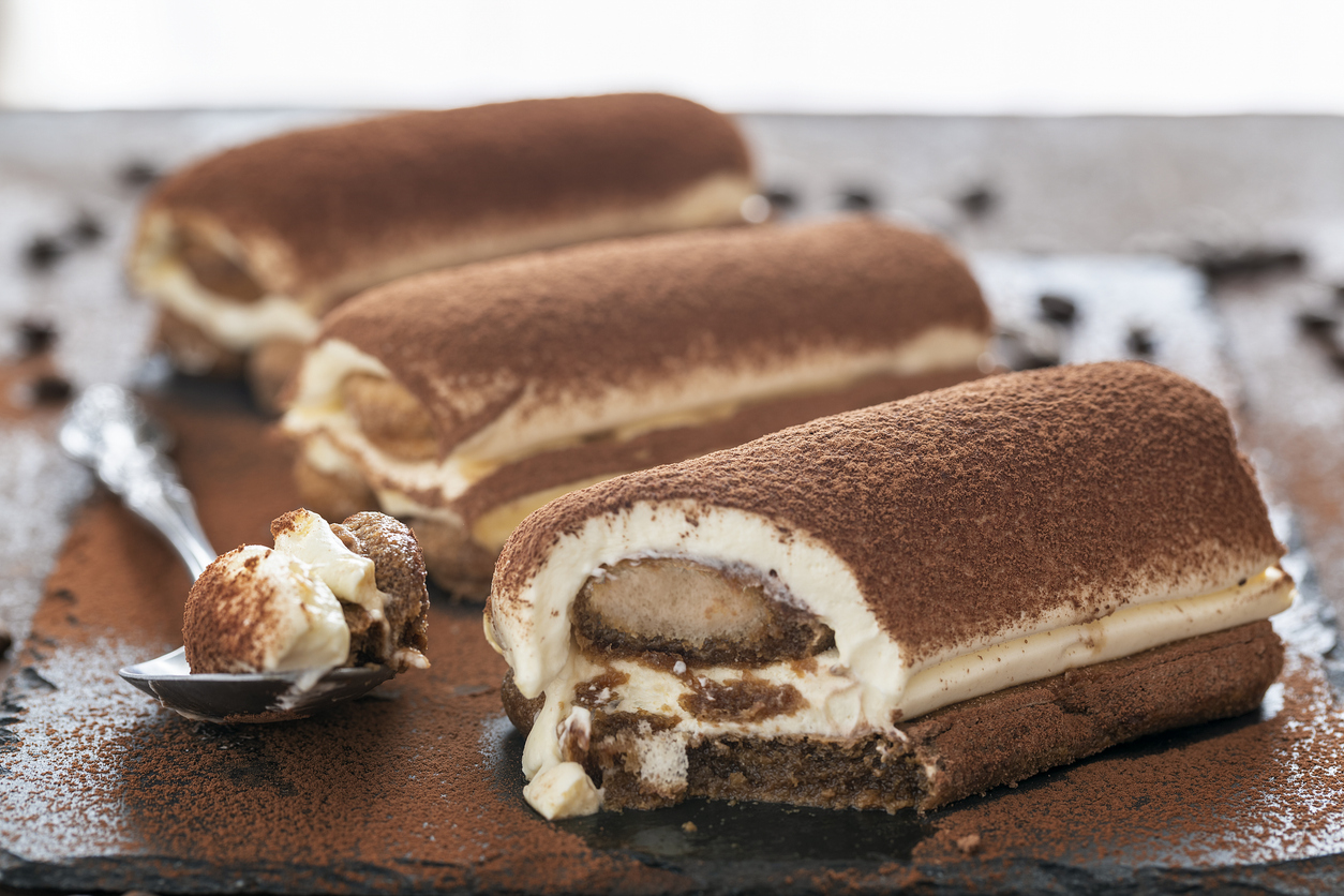 Aufgeschnittene Tiramisù-Stücke mit Kakaopulver und einem Löffel Creme im Vordergrund.
