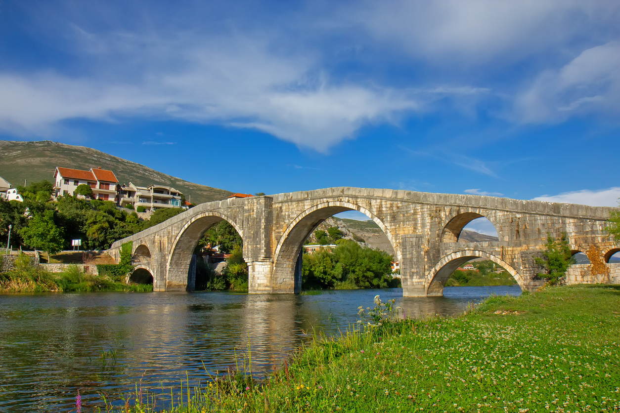 Steinerne Bogenbrücke in Trebinje überspannt die grüne Trebišnjica unter blauem Himmel.