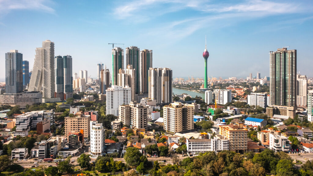 Panorama der Innenstadt von Colombo mit Wolkenkratzern, dem grünen Lotus Tower und dem Beira Lake unter blauem Himmel.