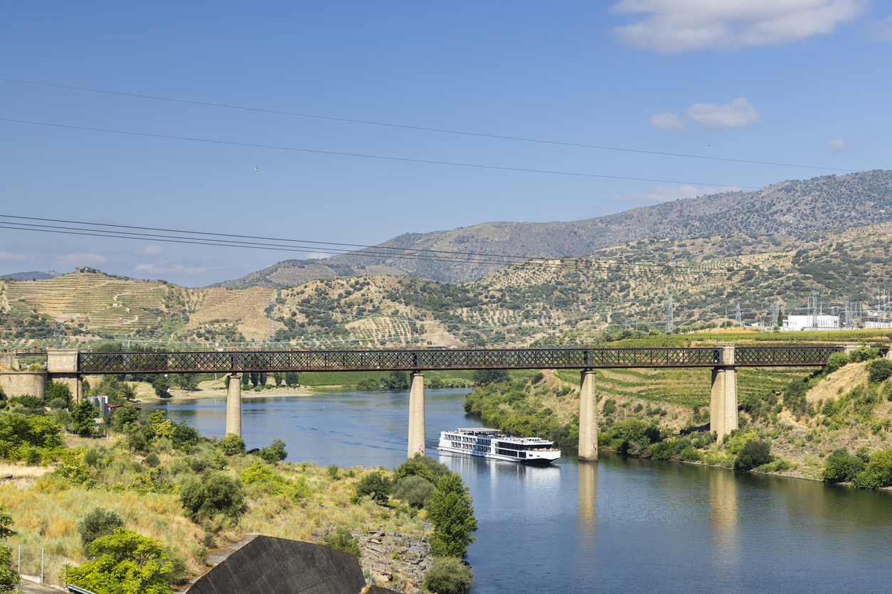 Ein Flusskreuzfahrtschiff passiert die hohe Eisenbahnbrücke bei Pocinho im Douro-Tal.