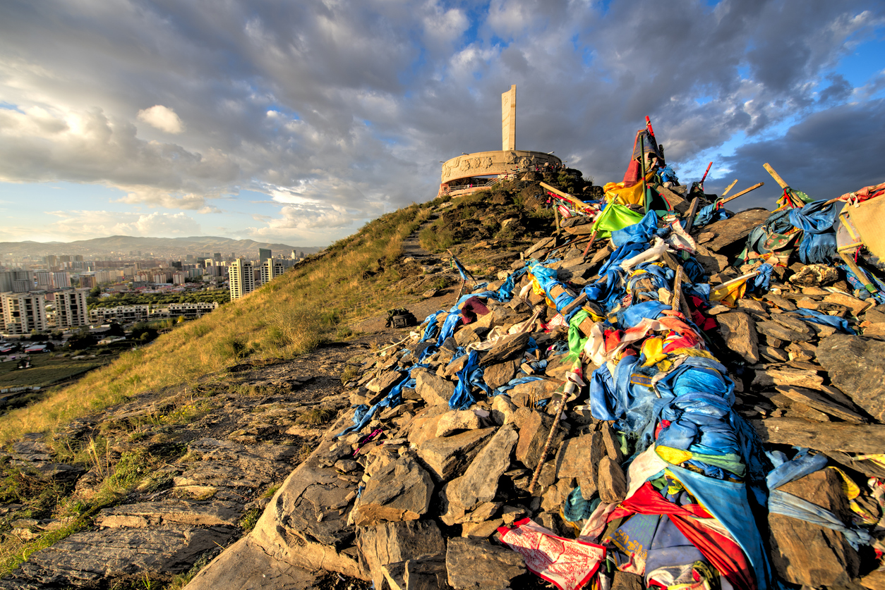 Zaisan-Denkmal über Ulaanbaatar. Steinhaufen mit blauen Gebetsschals im Vordergrund. Abendlicht und Skyline.