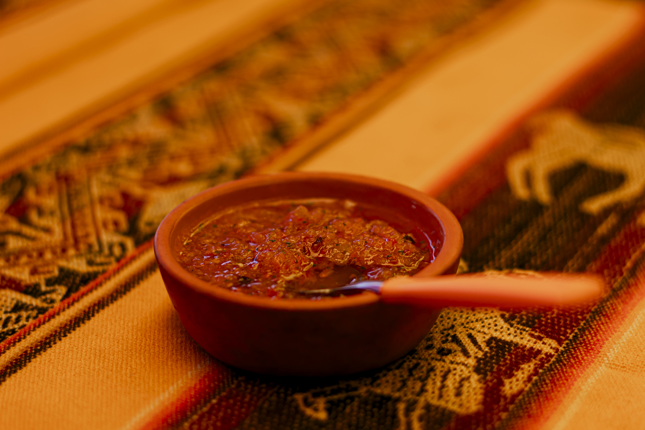 Tonschale mit roter Llajua-Salsa und Löffel auf bunt gewebter Andentischdecke.