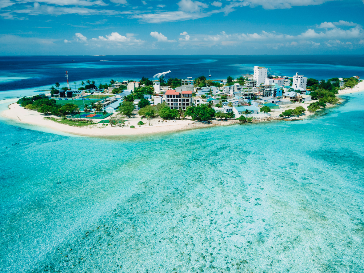 Luftaufnahme einer bebauten Insel mit Strand und flachem Riff.
