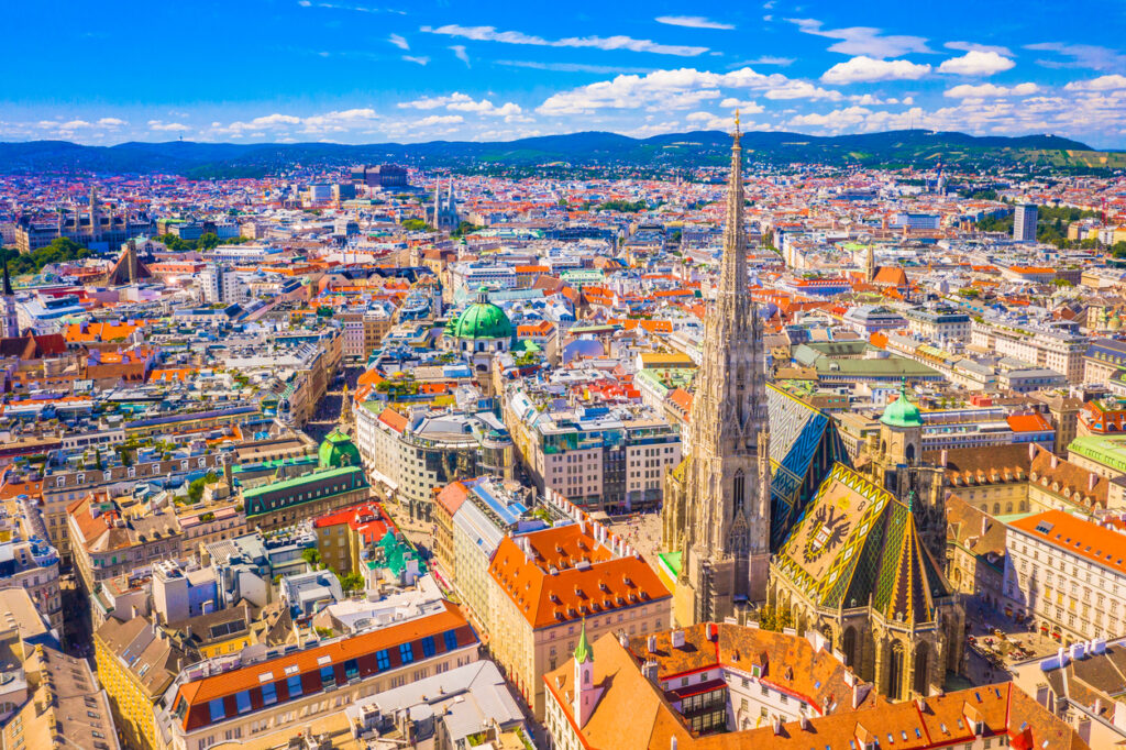 Luftaufnahme von Wien mit dem Stephansdom, buntem Ziegeldach und umliegender Innenstadt.