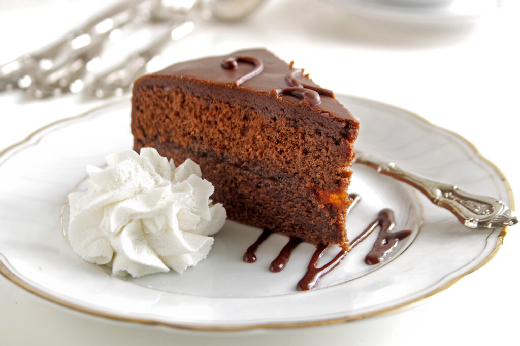 Stück Sachertorte mit Schokoglasur und Sahne auf weißem Teller