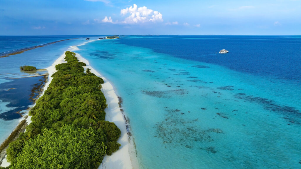 Luftaufnahme einer schmalen Insel mit weißem Strand, Palmen und klarem, türkisblauem Wasser.