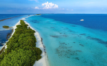 Luftaufnahme einer schmalen Insel mit weißem Strand, Palmen und klarem, türkisblauem Wasser.