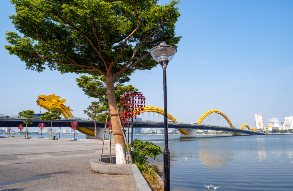 Gelbe Drachenbrücke überspannt einen ruhigen Fluss neben einer Promenade in der Stadt Da Nang.