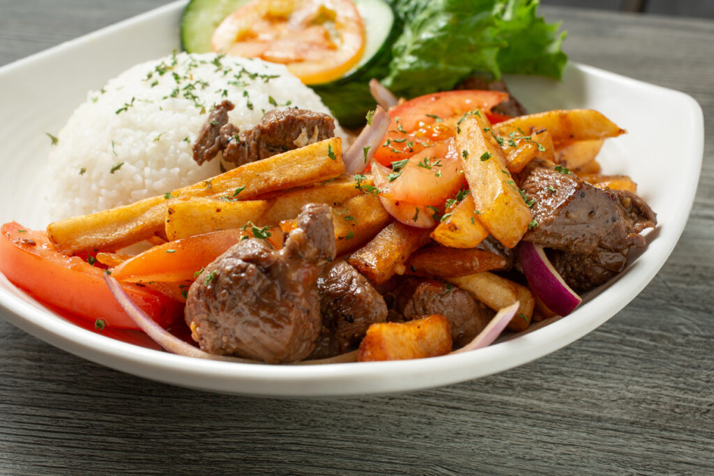 Teller mit Lomo saltado aus gebratenem Rindfleisch, Zwiebeln, Tomaten, Pommes frites und einem Häufchen Reis.