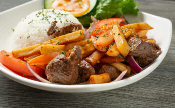Teller mit Lomo saltado aus gebratenem Rindfleisch, Zwiebeln, Tomaten, Pommes frites und einem Häufchen Reis.