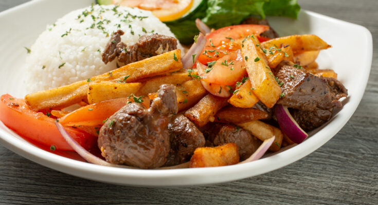 Teller mit Lomo saltado aus gebratenem Rindfleisch, Zwiebeln, Tomaten, Pommes frites und einem Häufchen Reis.