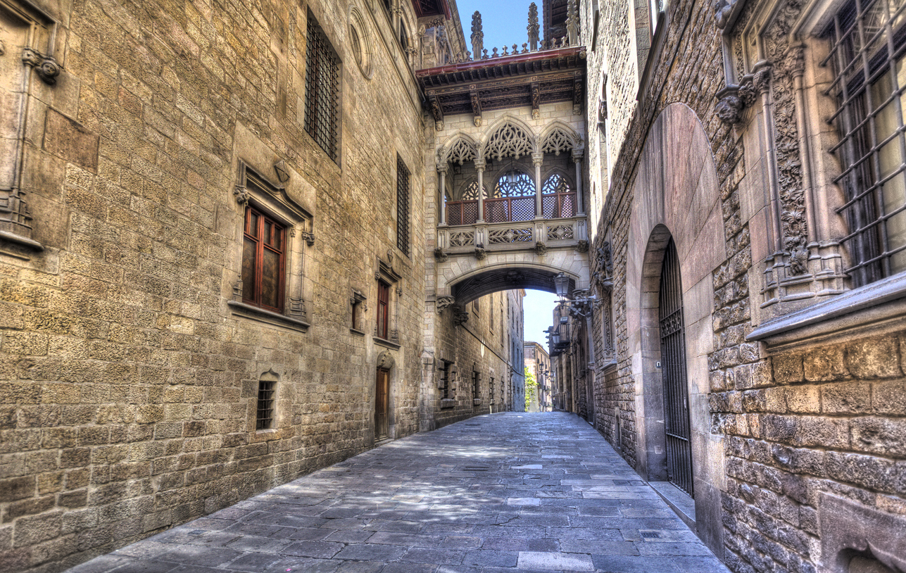 Leere Kopfsteinpflastergasse im Barri Gòtic in Barcelona mit dem neugotischen Pont del Bisbe zwischen historischen Fassaden.