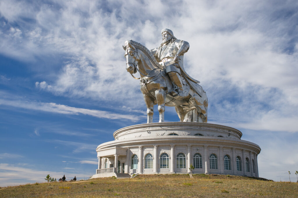 Silbern glänzende Reiterstatue von Dschingis Khan auf einem Rundbau unter blauem Himmel.