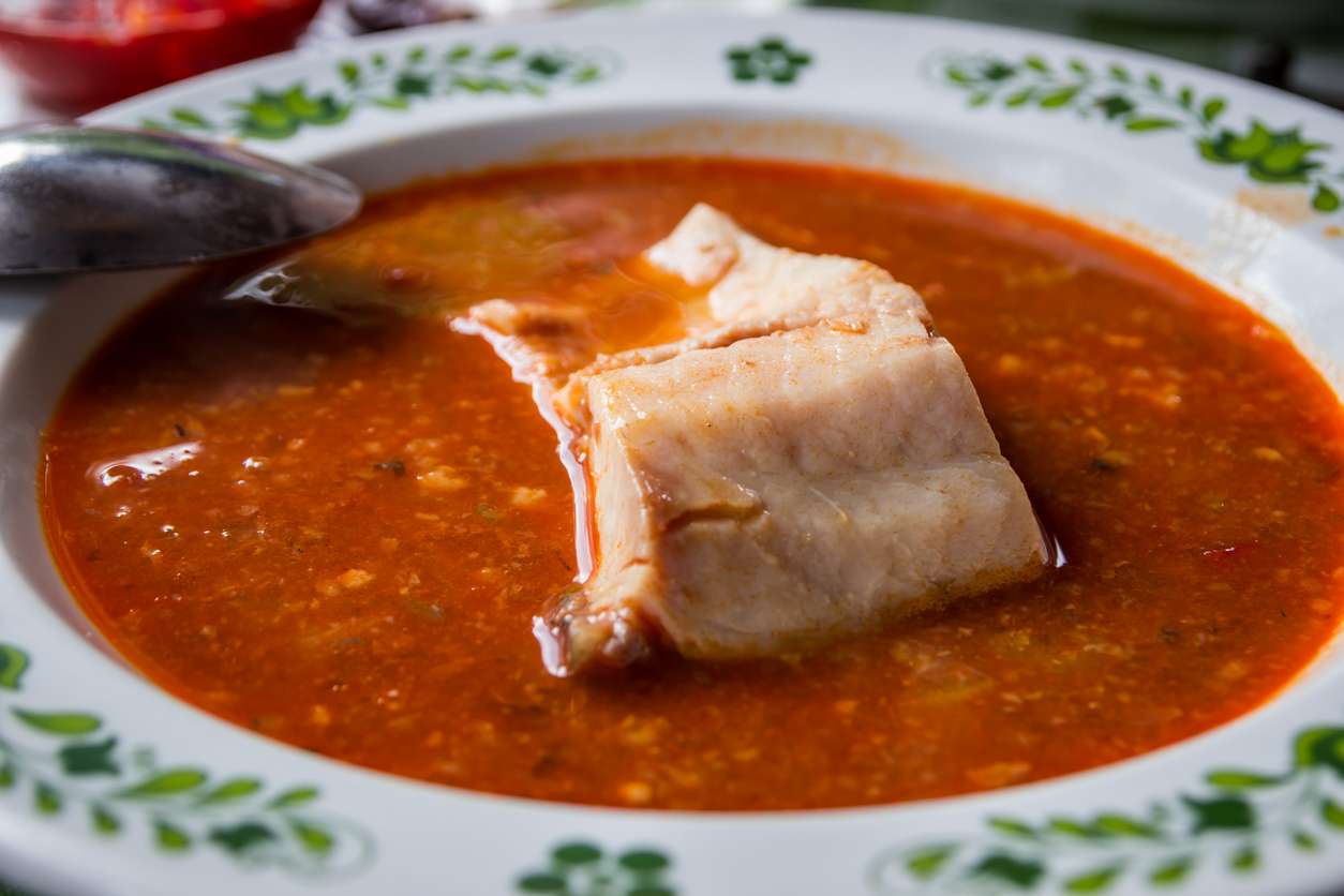 Rote Fischsuppe mit großem Fischstück in einem Teller.