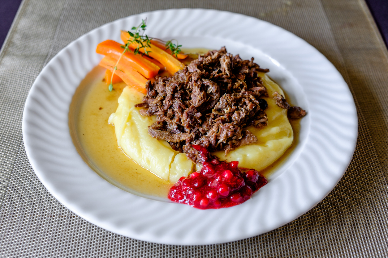 Teller mit Rentiergeschnetzeltem auf Kartoffelpüree, Preiselbeeren und Möhren.
