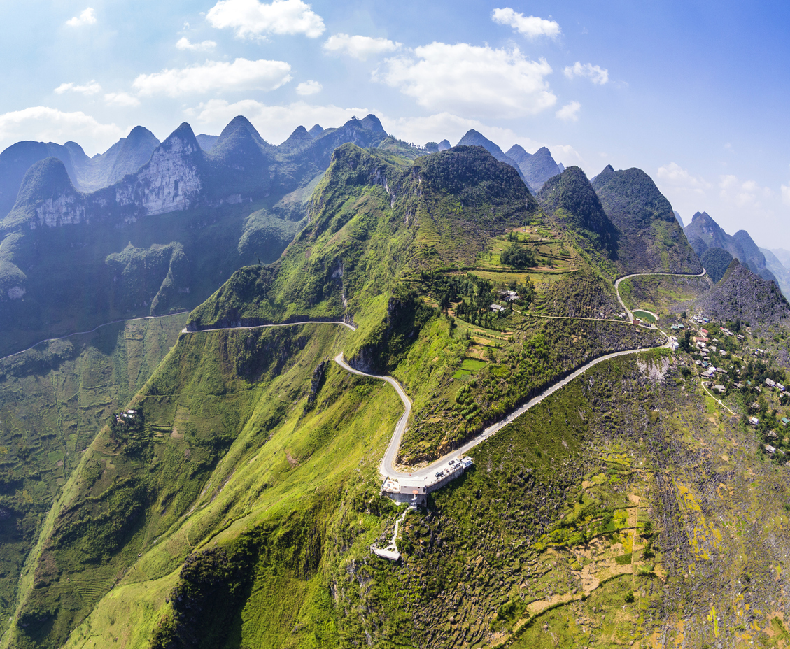 Luftaufnahme einer schmalen, serpentinenreichen Straße, die sich am Grat grüner Karstberge in Ha Giang entlangwindet.