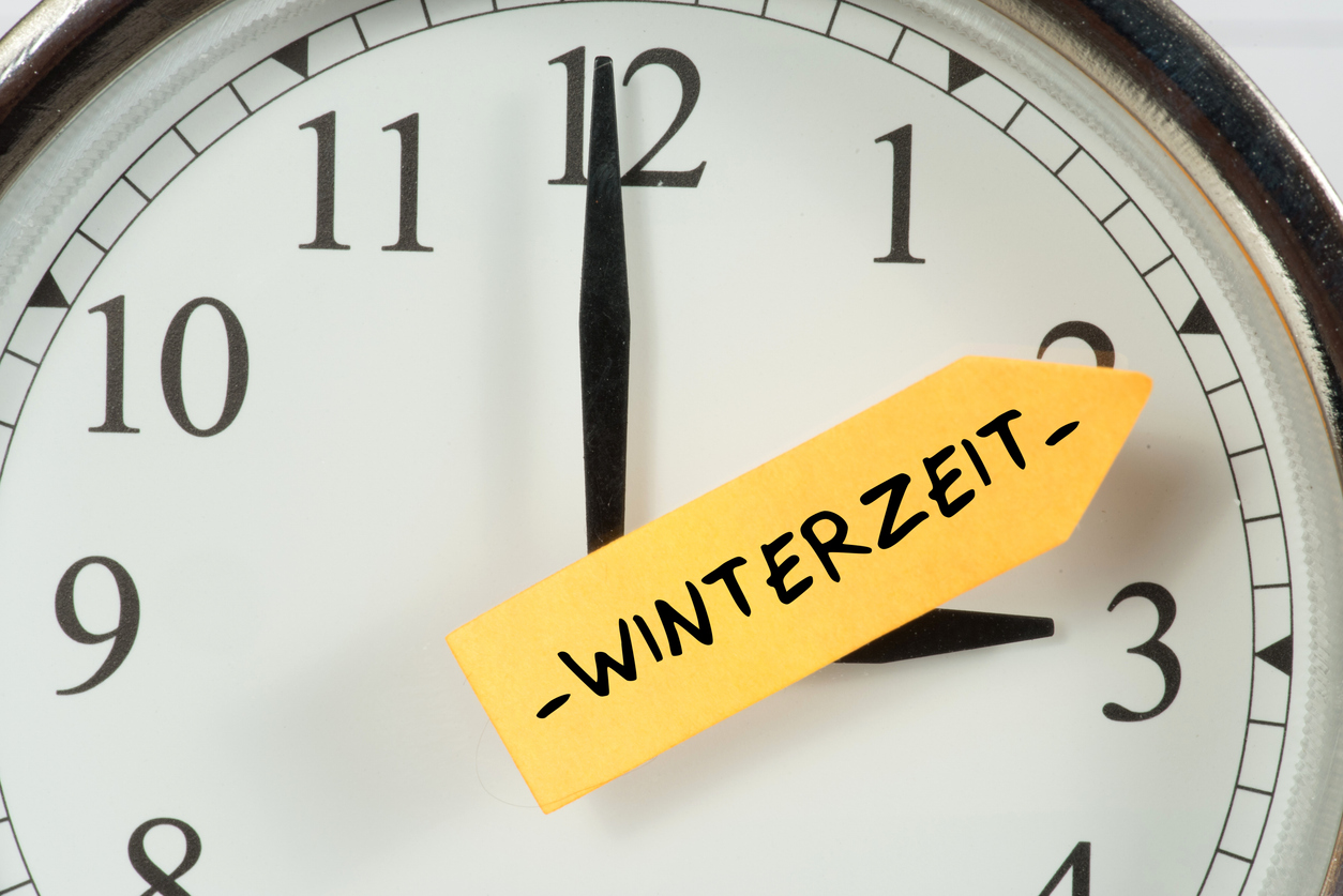 Nahaufnahme einer Uhr mit gelbem Pfeil-Sticker „Winterzeit“ als Hinweis auf die Umstellung.
