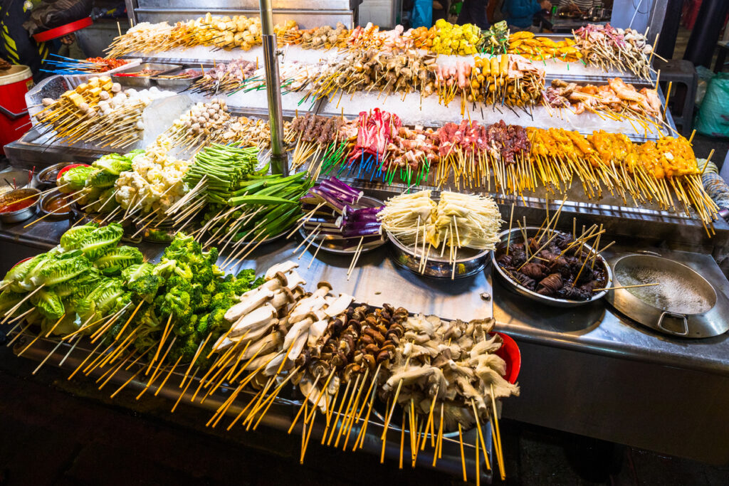 Straßenstand in Malaysia mit Reihen von Fleisch-, Meeresfrüchte- und Gemüsespießen.