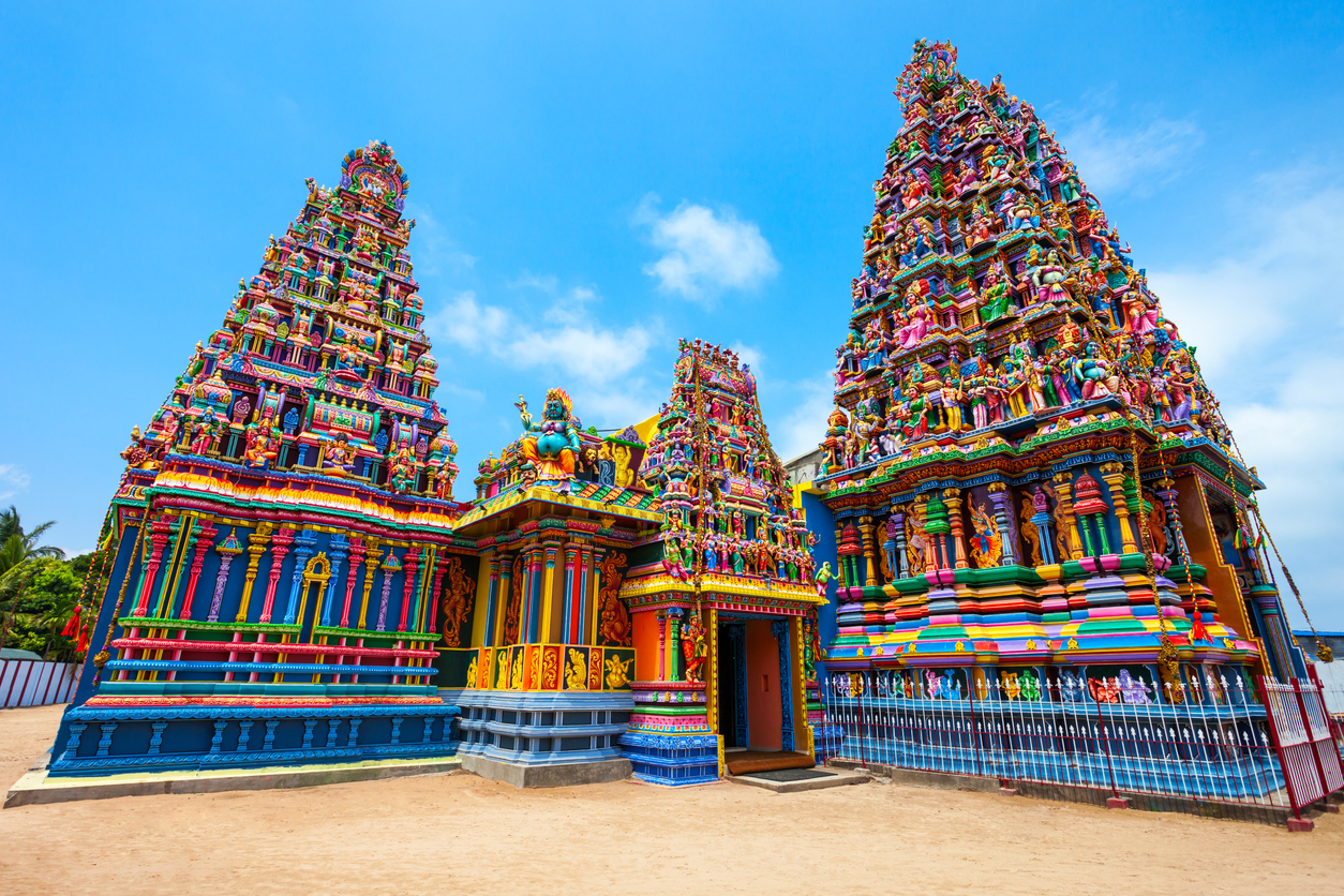 Kräftig farbige Gopuram-Türme eines hinduistischen Tempels in Trincomalee ragen detailreich verziert unter blauem Himmel auf.