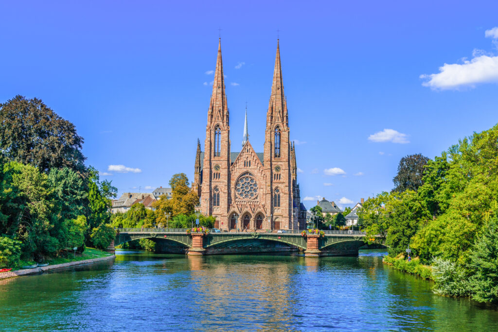 Neogotische Église Saint-Paul mit zwei Türmen über einer Brücke am Fluss Ill.