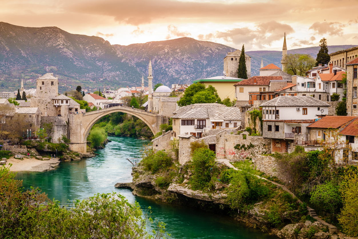 Die Bogenbrücke Stari Most spannt sich über die türkisfarbene Neretva, umgeben von steinernen Altstadthäusern und Minaretten.